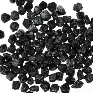 May include: A large pile of black tourmaline crystals, also known as schorl, on a white background.