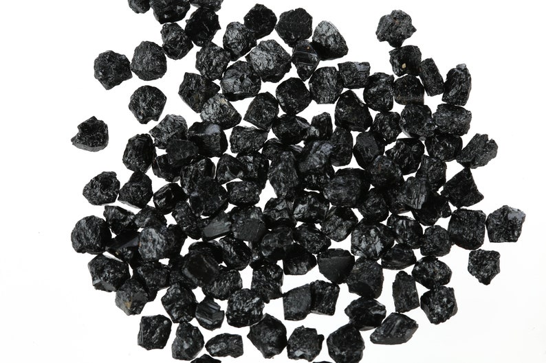 May include: A large pile of black tourmaline crystals, also known as schorl, on a white background.