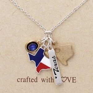 May include: Silver chain necklace with multiple charms, including a blue and red Texas state outline, a gold heart charm, and a silver charm with the word "Texas" on it. The necklace is on a brown background with the text "crafted with love".