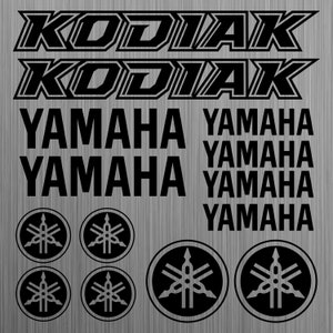 Könnte beinhalten: Ein Satz schwarzer und weißer Aufkleber für ein Yamaha Kodiak ATV. Die Aufkleber enthalten die Wörter "Kodiak" und "Yamaha" in einer fetten, klobigen Schriftart. Es gibt auch mehrere Yamaha-Logos mit einer stilisierten Stimmgabel.