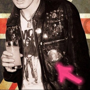 May include: Black leather jacket with metal studs and patches. The jacket is worn over a white graphic t-shirt. A glass of a light-colored beverage is held in the hand. The background has a vintage aesthetic.