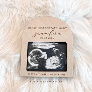 May include: Wooden frame with a black and white ultrasound image inside. The frame has the text "Handpicked for Earth by my grandma in Heaven" and "Baby Smith arriving July 2025".