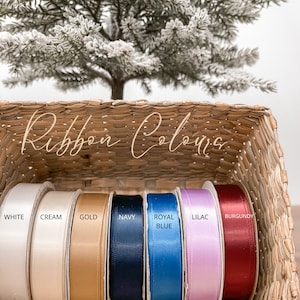 Puede incluir: Una cesta de mimbre muestra carretes de cinta de raso en varios colores: blanco, crema, dorado, azul marino, azul real, lila y burdeos. El texto "Ribbon Colors" est&aacute; escrito en la parte superior de la imagen.