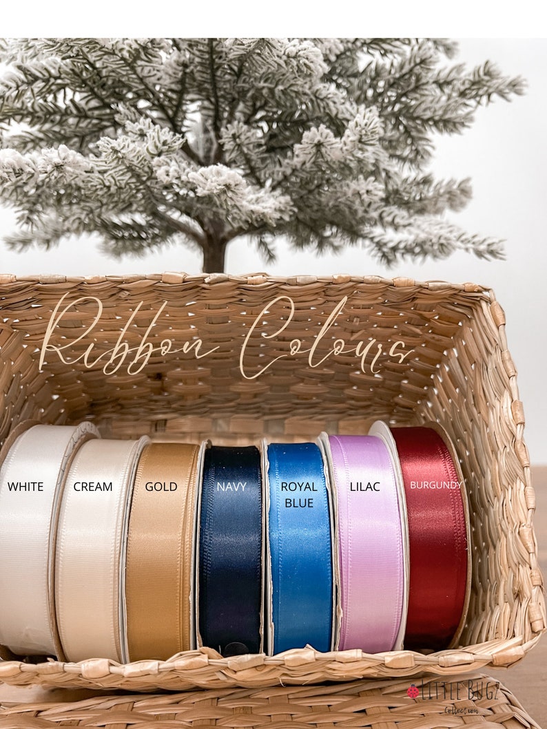 Puede incluir: Una cesta de mimbre muestra carretes de cinta de raso en varios colores: blanco, crema, dorado, azul marino, azul real, lila y burdeos. El texto "Ribbon Colors" est&aacute; escrito en la parte superior de la imagen.
