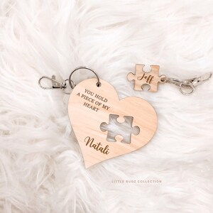 Peut inclure: Porte-clés en bois en forme de cœur avec une découpe en forme de pièce de puzzle et le texte "YOU HOLD A PIECE OF MY HEART" et "Natali". Un porte-clés en forme de pièce de puzzle séparé est gravé avec "Jeff". Les deux porte-clés ont des fermoirs argentés.