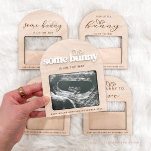 May include: Wooden pregnancy announcement frames with the text "Some Bunny Is On The Way" and "Our Little Bunny Is On The Way". Each frame holds a sonogram image. The bottom of the frame reads "Baby Miller Arriving November 2026".