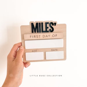 K&ouml;nnte beinhalten: Ein Holzschild mit dem Namen "MILES'" in schwarzen Buchstaben. Das Schild tr&auml;gt au&szlig;erdem die Aufschrift "ERSTER TAG VON" und hat leere Felder f&uuml;r Alter und Datum. Das Schild wird von LITTLE BUGZ COLLECTION hergestellt.