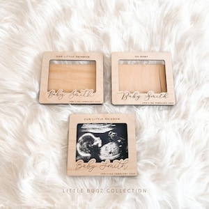 May include: Three wooden picture frames with a white background. The frames are decorated with the text "Our Little Rainbow" and "Oh Baby". The frames are designed to hold ultrasound photos and have the text "Baby Smith" and "Arriving February 2025" engraved on them.