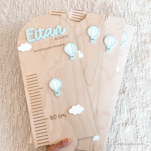 May include: A light-colored wooden growth chart featuring the name Eitan Ronen in blue 3D lettering, the text loved beyond measure, white clouds, and light blue hot air balloon accents, with a measurement scale ending at 160 cm.