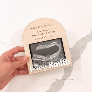 May include: A wooden ultrasound photo frame with the text "MADE WITH LOTS OF love AND A LITTLE BIT OF science". The frame has a rectangular opening for the ultrasound image and a white nameplate that says "baby Smith".