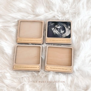 May include: Four wooden picture frames with gold accents and engraved text. The frames are arranged in a square shape. The text on the frames reads: "Life begins and love never ends", "After every storm there is a rainbow", "You are our greatest adventure", and "You are so loved little one".