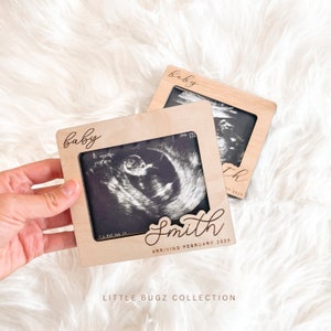 May include: A wooden frame with a cutout for an ultrasound image. The frame is engraved with the words "baby" and "Smith arriving February 2025".