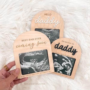 May include: Wooden pregnancy announcement plaques with ultrasound images. The plaques say "Hello Daddy", "Best Dad Ever coming soon", and "Promoted to Daddy". Each plaque includes the text "I can't wait to meet you" and the baby's due date.
