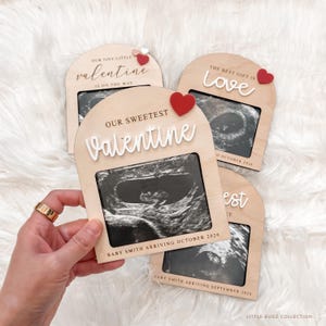 May include: Wooden pregnancy announcement frames with sonogram images. The frames have arched tops and feature the words "Our Sweetest Valentine," "Our Tiny Little Valentine is on the Way," and "The Best Gift is Love." Each frame includes a red heart accent and the baby's expected arrival month and year.
