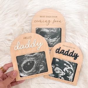 May include: Three wooden pregnancy announcement plaques with ultrasound images. The plaques say "Hello Daddy," "Promoted to Daddy," and "Best Dad Ever." Each plaque includes the text "I can't wait to meet you" and the baby's due date.