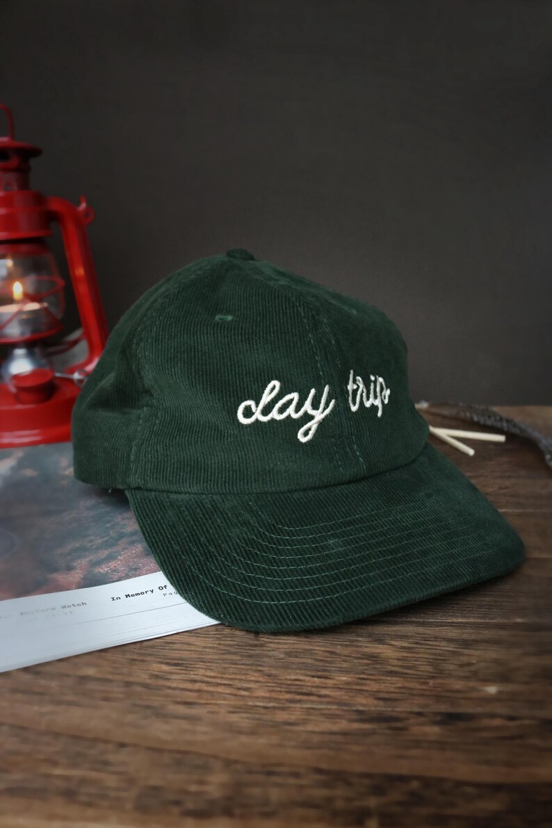 May include: A dark green corduroy baseball cap with white embroidery that reads "day trip".
