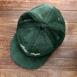 May include: A dark green corduroy baseball cap with a white embroidered design that says "day trip".