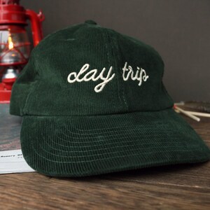 May include: A dark green corduroy baseball cap with the text "clay trip" embroidered in white on the front.