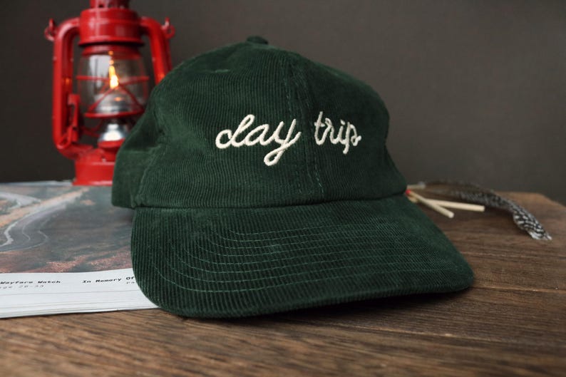 May include: A dark green corduroy baseball cap with the text "clay trip" embroidered in white on the front.