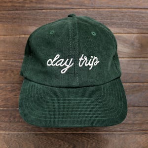 May include: A dark green corduroy baseball cap with white embroidery that reads "clay trips".