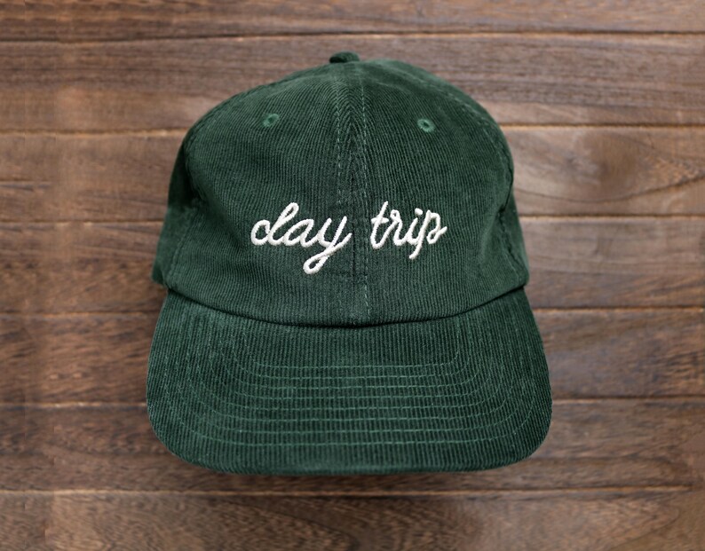 May include: A dark green corduroy baseball cap with white embroidery that reads "clay trips".