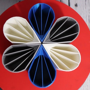 May include: A set of five 3D printed pen holders in the shape of a flower. The holders are in shades of blue, white, and gray.