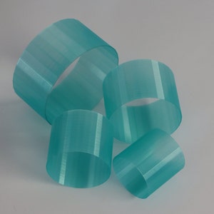 Peut inclure: Quatre anneaux en plastique translucides de couleur turquoise de tailles différentes. Les anneaux sont empilés les uns sur les autres.
