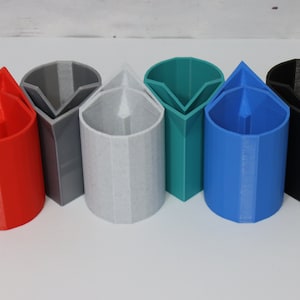 May include: Six 3D printed pencil holders in different colours: red, grey, light grey, teal, blue, and black. Each holder has a triangular opening at the top.