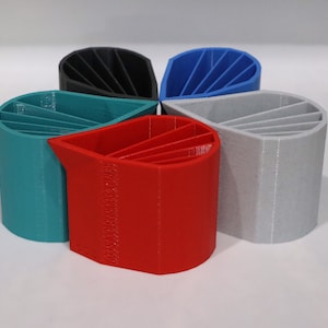 May include: Five 3D printed pencil holders in different colors: teal, red, gray, black, and blue. Each holder has a unique design with multiple slots for pencils.