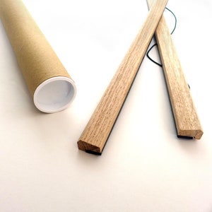 May include: Two wooden poster hangers with black magnetic strips on the back. The hangers are crossed and tied together with a string. The hangers are packaged in a brown cardboard tube.