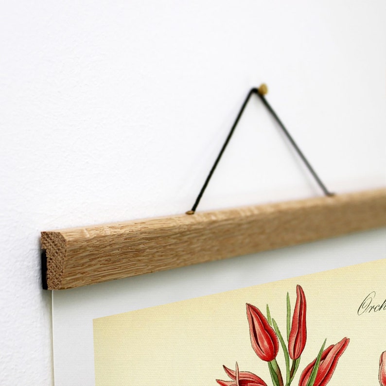 May include: A wooden poster hanger with a black string hanging from it. The hanger is made of natural wood and has a simple design. The string is attached to the hanger with two brass-colored metal hooks.