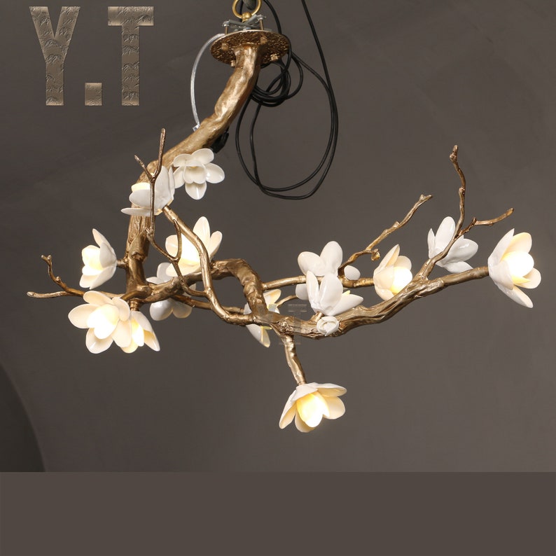 May include: A decorative chandelier in a branch design with white flower-shaped lights. The fixture has a gold-colored finish and includes the letters "Y.T" in the upper left corner.