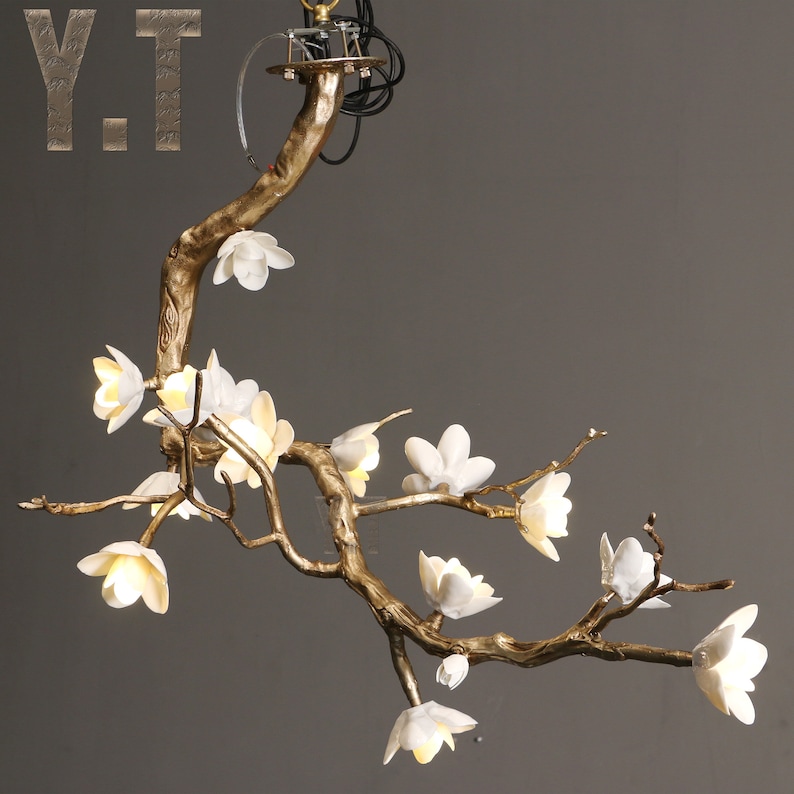 May include: A decorative chandelier in the shape of a tree branch, with white flower-shaped lights. The branch is a gold color, and the fixture has the letters "Y.T." in the upper left corner.