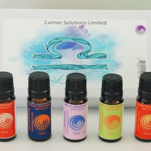 May include: Five small essential oil bottles with black caps and colorful labels are arranged in front of a box. The labels display the text "Calmer Solutions" and various essential oil names. The box has the text "Calmer Solutions Limited" and a Libra symbol.