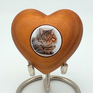May include: A wooden heart-shaped urn with a photo of a tabby cat. The urn is on a metal stand. "Stand not included" is written on the stand.