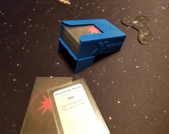 May include: A blue card game deck box with a clear top and a red star logo. The box is labeled "X-Wing". A card with the text "Panicked Pilot" and the text "Gain 2 stress tokens. Then repair this card." is visible.