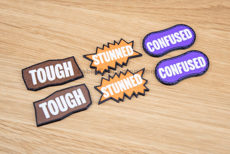 Puede incluir: Seis parches de fieltro con diferentes palabras. Dos parches marrones dicen "TOUGH", dos parches naranjas dicen "STUNNED" y dos parches morados dicen "CONFUSED".
