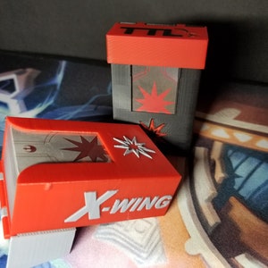 May include: Red and gray storage boxes with white lettering and starburst designs. One box reads "X-WING" and the other reads "TTL". The boxes are on a patterned surface.