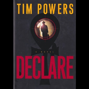 May include: Book cover for "DECLARE" by Tim Powers. The cover features a dark background with the title in red and the author's name in yellow. A silhouette of a person is seen through a crosshair.