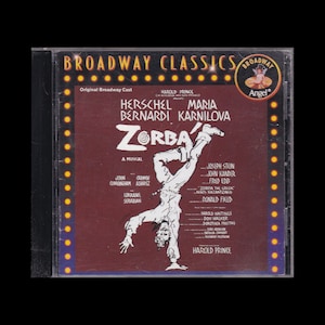 May include: A CD case for the Broadway musical "Zorba," featuring Herschel Bernardi and Maria Karnilova. The cover is burgundy with white text and a stylized illustration of a man doing a handstand. The "Broadway Classics" logo is at the top.