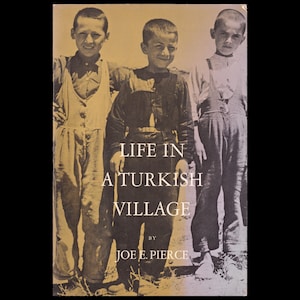 May include: A sepia-toned book cover titled LIFE IN A TURKISH VILLAGE BY JOE E. PIERCE. The cover features a black and white photograph of three young children standing side by side, wearing shirts and overalls in a rural outdoor setting.