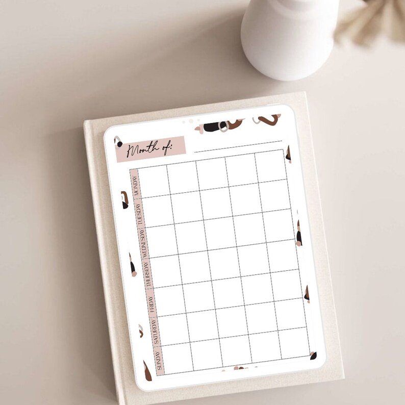 May include: A printable monthly calendar planner with a white background and black grid lines. The calendar has a pink header with the text "Month of:" and a brown and black abstract design on the border.