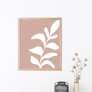 May include: A framed print featuring a white stylised leaf design on a light pink background.