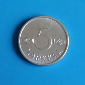 May include: A silver Finnish 5 Markka coin with the number "5" and the word "MARKKA" inscribed around the edge.