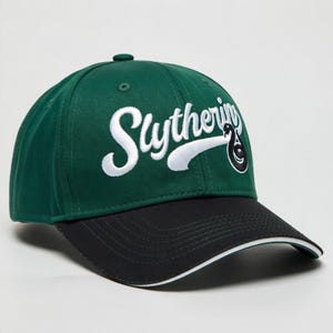 May include: Green baseball cap with a black brim and white trim. The word "Slytherin" is embroidered in white script across the front, with a stylized snake emblem. A classic, adjustable hat.
