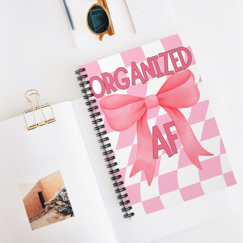 May include: A pink and white spiral notebook with a pink bow and the text "ORGANIZED AF".