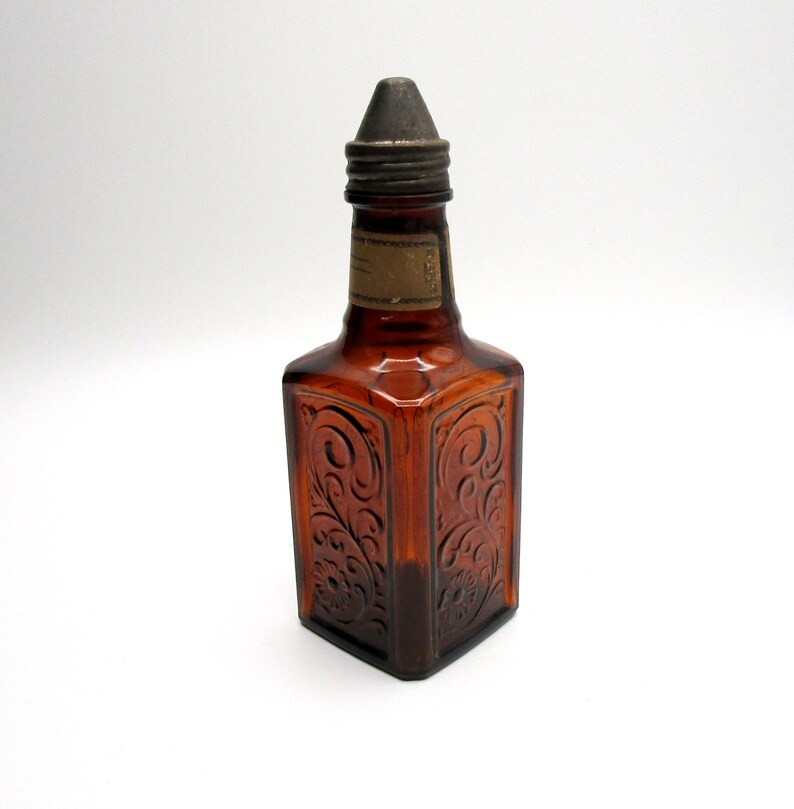 Puede incluir: Una botella de vidrio marr&oacute;n con un tap&oacute;n de metal y un dise&ntilde;o floral en relieve. La botella tiene una etiqueta en la parte delantera.