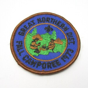 May include: A blue and brown embroidered patch with the text "Great Northern Dist. Fall Camporee 1973" and a depiction of two figures sitting around a campfire.