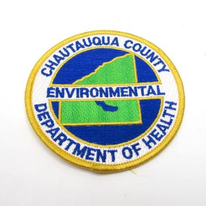 May include: Embroidered patch with the text "Chautauqua County Environmental Department of Health" in a circular design. The patch features a blue and green graphic with a gold border and white lettering.