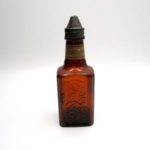 Puede incluir: Una botella vintage de vidrio &aacute;mbar con un tap&oacute;n de metal. La botella tiene un dise&ntilde;o floral en relieve y una etiqueta que dice "Stato" en cursiva.